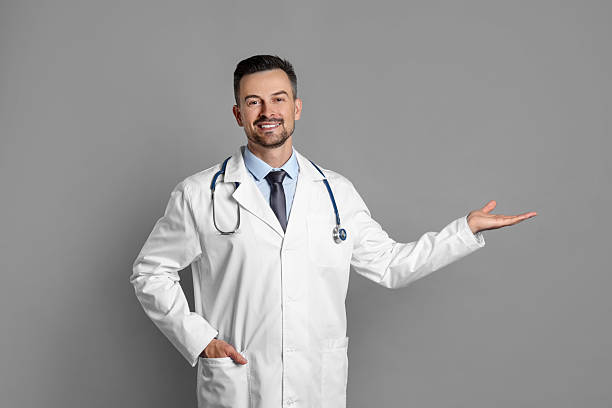 istock Smiling doctor with stethoscope pointing at something on grey background 2216276496