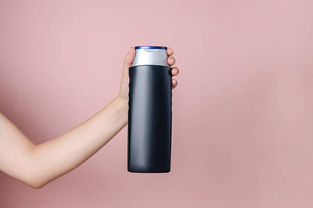 istock Woman's hand holding shampoo bottle on the solid pink background. Cosmetics product package, your brand, spa. Space for text 2216276633