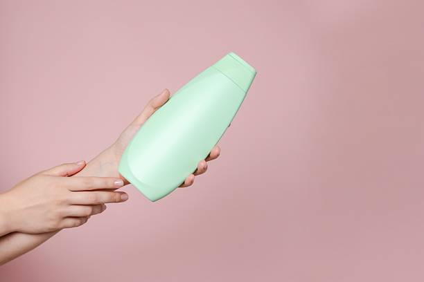 istock Elegant hand with shampoo light bottle isolated on solid pink background. Package for cosmetics product, your brand, spa, beauty. Space for text 2216276634