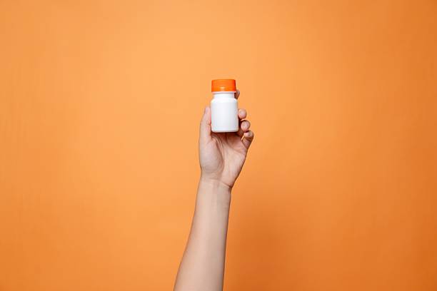 istock Blank bottle mockup in hand on orange background. Package for cosmetics product, nutritional supplements, vitamins, spa, beauty and luxury. Space for text 2216276648