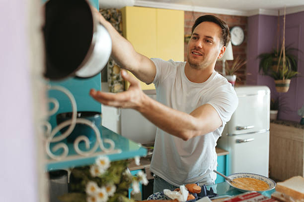 Smiling man reaching for frying pan while preparing breakfast in a domestic kitchen