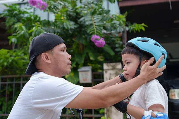 Asian father assists his young son with a bicycle helmet, preparing for a bicycle ride.