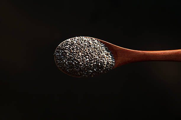 Close-up of chia seeds resting in a wooden spoon, isolated against a dark background. A healthy superfood rich in fiber and omega-3.