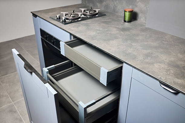 istock Pull out rack cabinets drawers. Flush up slip handle finger pull handle of drawers for dishes, compact high pressure laminate HPL countertop, black glass gas stove cooker hob with two burners. 2216286044