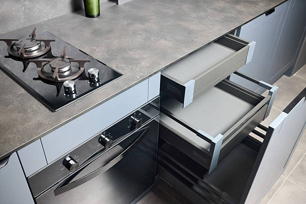 istock Pull out rack cabinets drawers. Flush up slip handle finger pull handle of drawers for dishes, compact high pressure laminate HPL countertop, black glass gas stove cooker hob with two burners. 2216286051