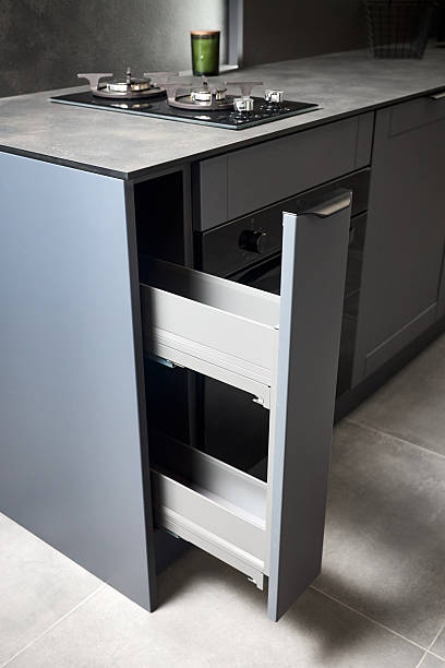 istock Vertical pull out rack cabinet drawer. Flush up slip handle finger pull handle of drawers for dishes, compact high pressure laminate HPL countertop, black glass gas stove cooker hob with two burners. 2216286068