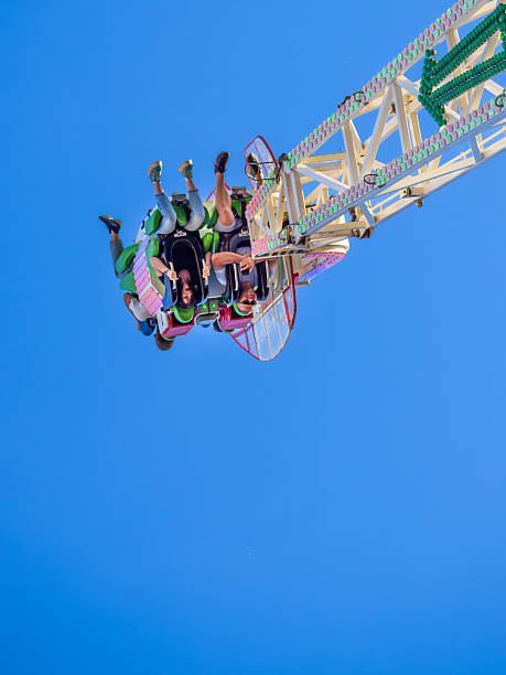 Villach, Austria - July 29, 2025: Excited riders experience a thrilling amusement park ride, suspended upside down against a vibrant blue sky, showcasing joy and exhilaration
