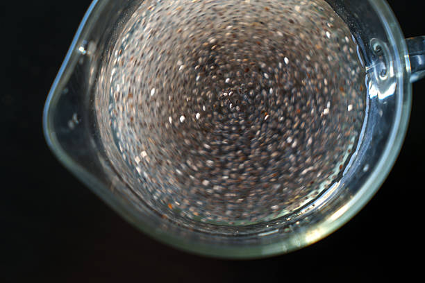 Top-down view of chia seeds being stirred in water inside a transparent glass container, creating a swirling motion effect.