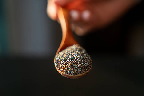 Close-up image of chia seeds in a wooden spoon, held by hand against a dark blurred background. A natural, healthy ingredient concept in soft lighting.