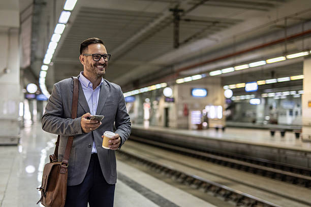 istock Smiling businessman waiting for train, holding coffee and using smartphone 2216296142