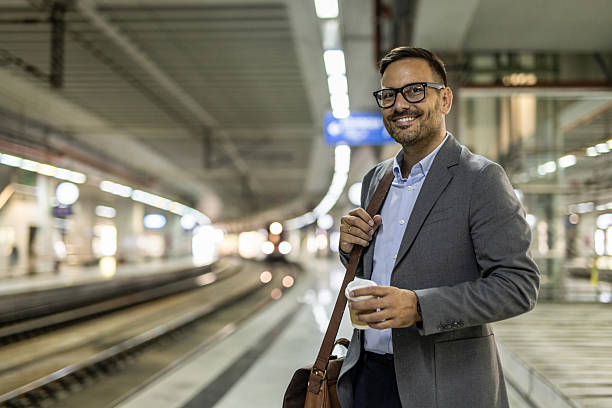 istock Smiling businessman waiting for train at station with coffee 2216296199
