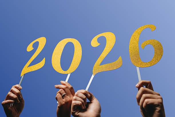 istock Hands holding golden numbers 2026 against blue sky 2216296529