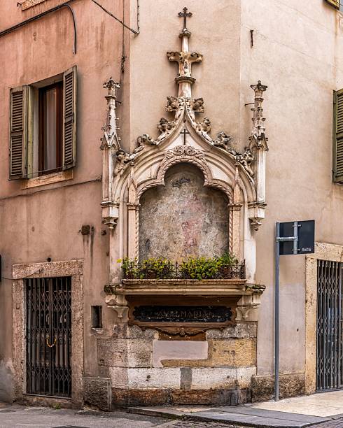 Stone column with carved Madonna relief stands in Verona's main square, framed by frescoed Renaissance facades and pastel historic buildings