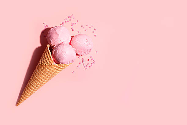 Strawberry pink ice cream scoops with heart shape sprinkles in waffle cone on pink background, creative design with hard light, copy space.  Summer berry ice cream trendy concept.