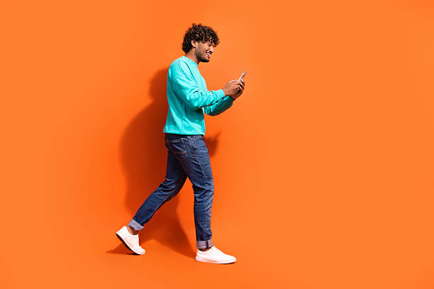 istock Side profile photo of young positive happy guy walking using smartphone texting girlfriend for a date isolated on orange color background 2216315700