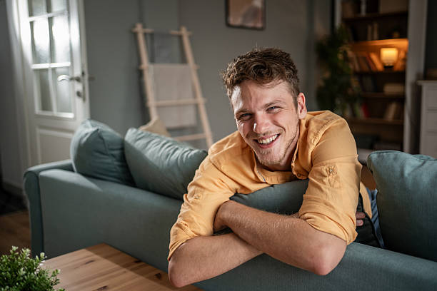istock Young man relaxing on sofa at home smiling at camera 2216323525