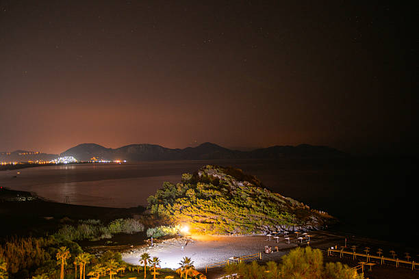 BODRUM, TURKEY - JUNE 29: People walk near a brightly lit digital billboard displaying an animated advertisement on June 29, 2025, in Bodrum, Turkey. The area is surrounded by restaurants, motorbikes, and palm trees, illustrating the city's vibrant summer nightlife.