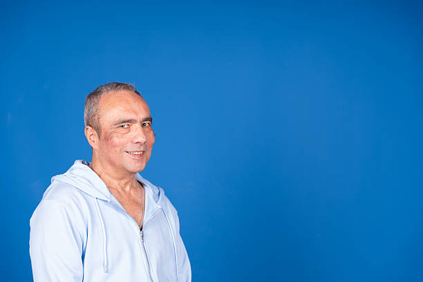 Smiling mature adult man in casual attire standing confidently against a solid blue background, conveying positivity and approachability. Ideal for professional contexts