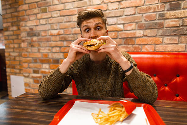 istock young guy eats a hamburger and french fries in a cafe 2216333539