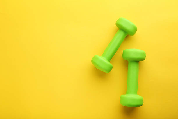 istock Green dumbbells on yellow background 2216333852