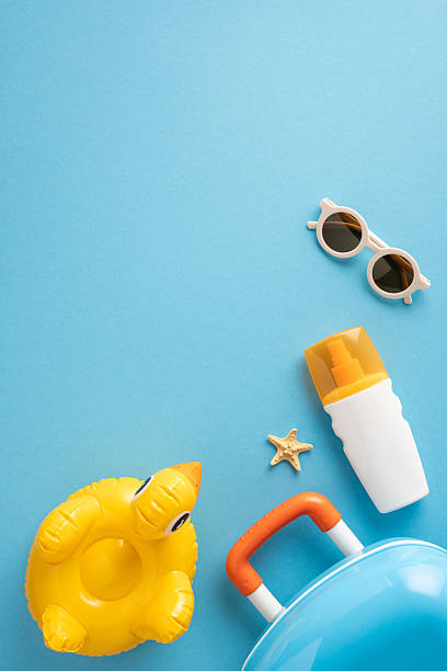 istock Flat lay vertical composition featuring summer travel accessories including a suitcase, sunscreen, sunglasses, starfish, and inflatable duck on a blue background, evoking feelings of vacation 2216334947