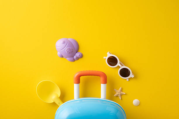 istock A vibrant yellow backdrop features beach toys, sunglasses, a small suitcase, and summer objects 2216334973