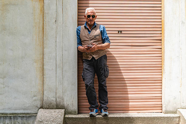 elegant middle-aged man wearing sunglasses using mobile phone standing on concrete staircase outdoors