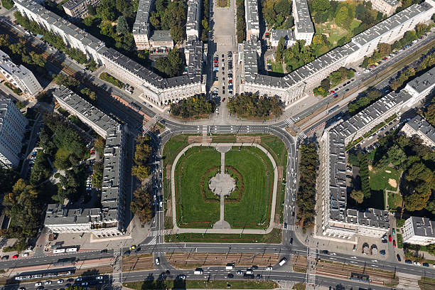 Aerial view of a large, symmetric residential district with white apartment buildings, streets and green town square.