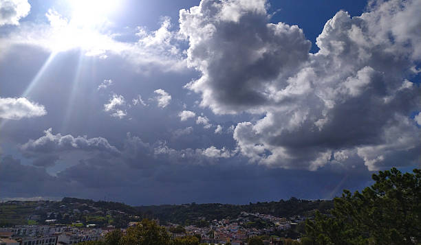 Dramatic skyscape with sunbeams piercing through cumulus clouds over a distant town. Evokes hope, change, natures power. Ideal for weather, travel, or inspirational themes.