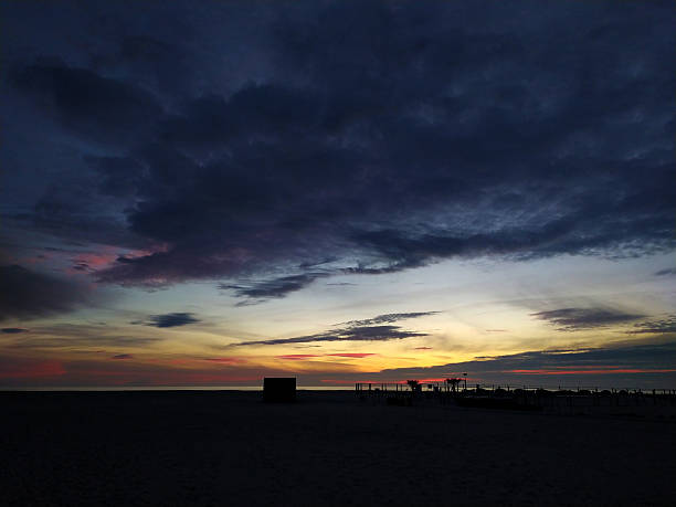 Dramatic coastal sunset with a dark, moody sky over a tranquil beach. Evokes peace, reflection, and the beauty of natures raw power. Perfect for travel, wellness, or inspirational themes.
