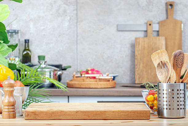 istock Kitchen table with cutting board, spice grinder, vegetables and utensils, countertop with pans on induction hob, trays etc. 2216359500