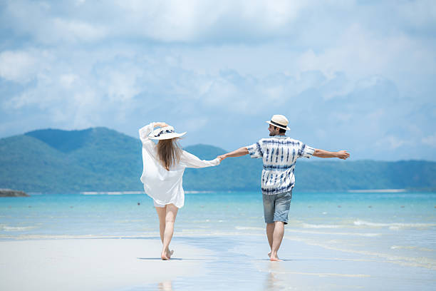 Young couple on vacation on a white sandy beach, clear sky and sea