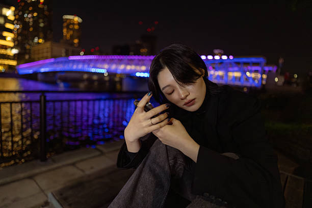 Young woman using resting / meditating by the river at night waterfront city