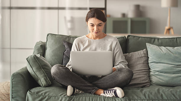 istock Woman sitting on sofa and using laptop at living room 2216381321