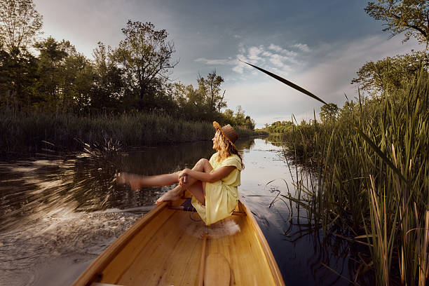 Happy woman having fun while splashing water with her leg from a canoe on a lake. Copy space. Blurred motion.