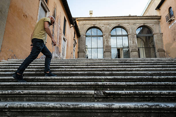A man climbs a worn historic staircase in Rome, surrounded by weathered ochre buildings and arched windows, evoking the charm and timelessness of the Eternal City.