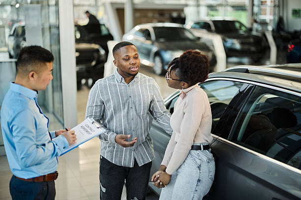 istock Black couple talking while standing with a car salesman in a showroom. 2216387414
