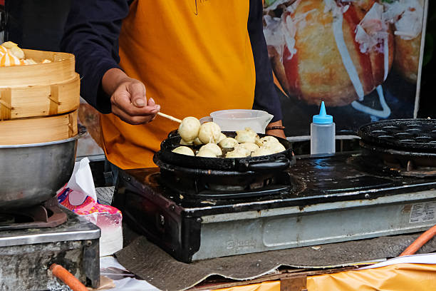 A Man prepare a Takoyaki on hot pan. Process to cooking fried balls with octopus in local street food.