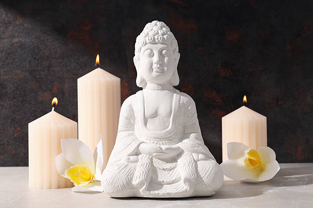 istock White Buddha statue, flowers and candles on dark background 2216391661