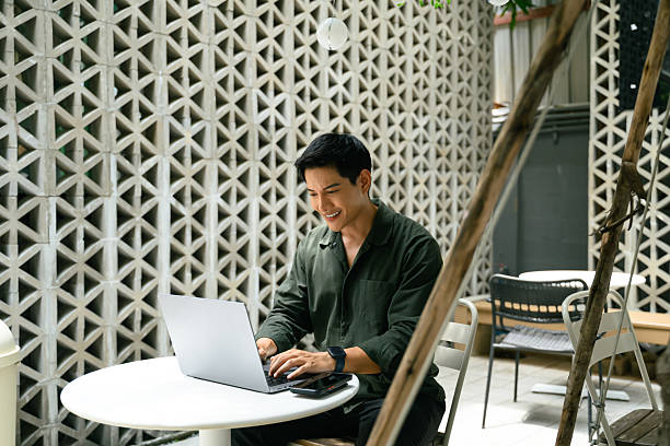 istock Smiling man working remotely on a laptop at a modern outdoor cafe 2216394751