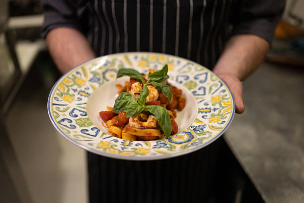 Midsection shot of unrecognizable chef holding pasta dish in restaurant kitchen
