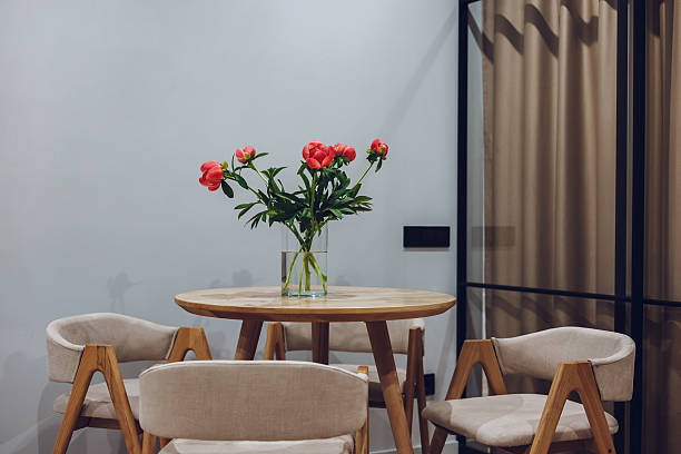 A charming interior features a table with vibrant red peonies, creating a cozy atmosphere. Vibrant red peonies in a glass vase adorn a wooden table. Soft, natural light and cozy interior design elements create a warm atmosphere.
