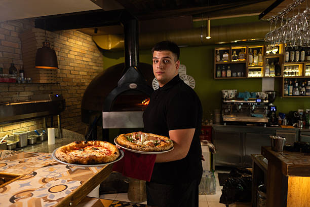 Chef holding two freshly baked pizzas while working in restaurant kitchen