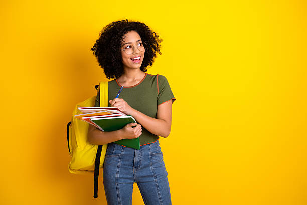 istock Young female student with notebooks and backpack standing against a yellow background, smiling with confidence and style 2216400265