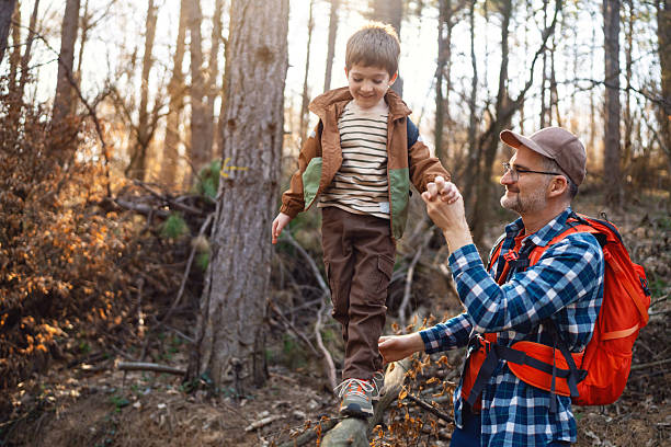 istock A father holds his son while he's balancing on a tree trunk during a hike in the woods 2216400371