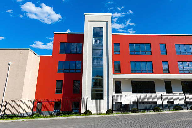 istock Front view of a modern red and white building with black window frames under a bright blue sky with scattered clouds. 2216402792