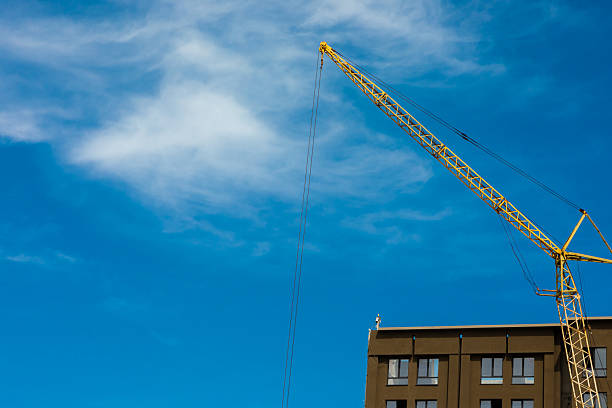 Yellow construction crane extending above a modern building under a vibrant blue sky with wispy clouds.