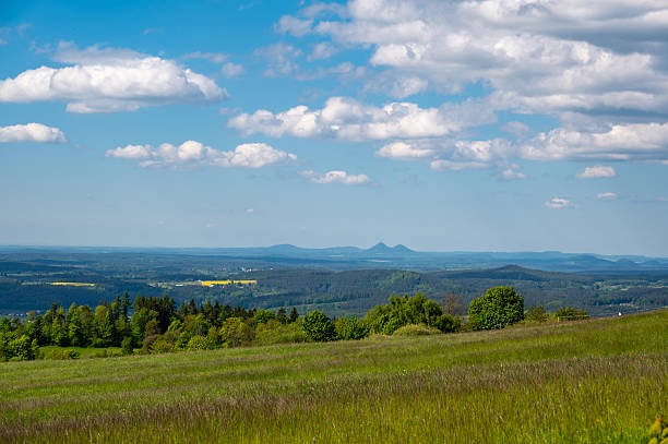 istock Panoramic view of green fields and forested hills near Jested, with the sharp peak of Ralsko mountain visible in the distance under a blue sky with scattered clouds. 2216408775
