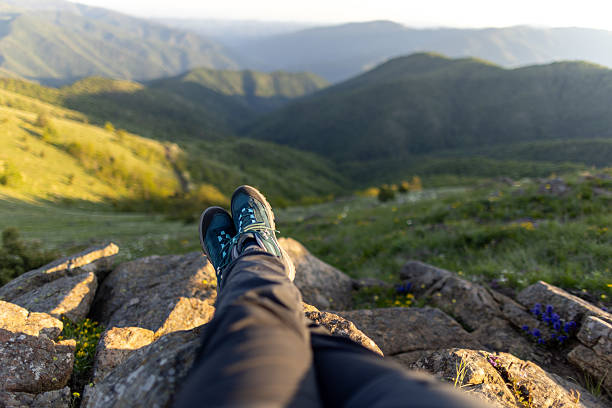 Mature woman taking a break from hiking to admire the view. The nature around her is amazing, it's a beautiful spring sunny day. She is watching sunset.