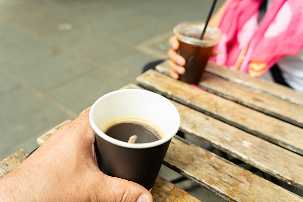 Close-up of a hand holding a disposable coffee cup on a wooden table, sharing a moment with a friend